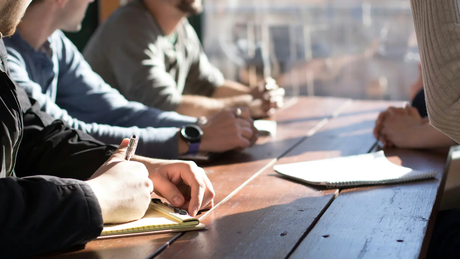 people sitting on chair in front of table while holding pens during daytime
